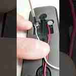Close-up of a person using a small screwdriver to work on a device's internal wiring, with red and white wires visible.
